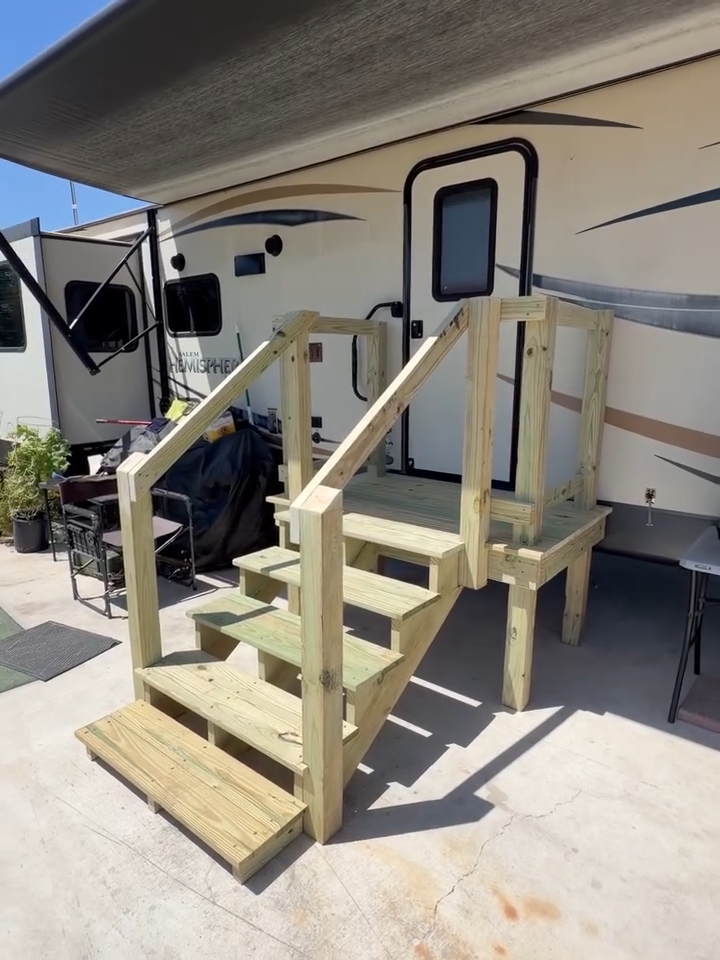 Wooden staircase with railings leading to an RV doorway under an awning