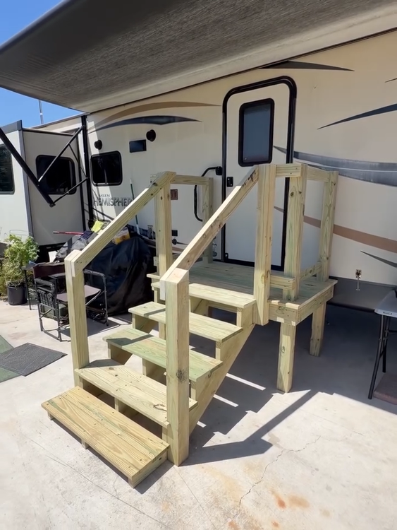 Wooden accessibility stair/ramp structure beside an RV under a covered awning