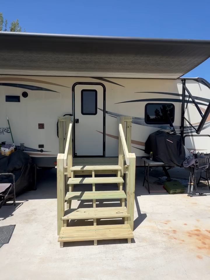 RV entry with portable wooden steps under an awning, parked on a concrete pad.