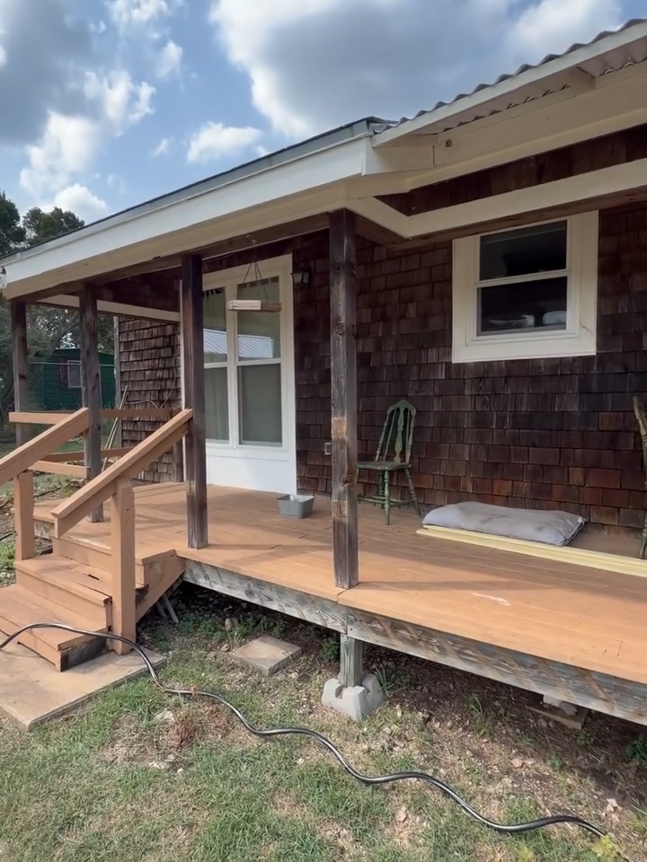 Wooden house porch with steps, railing, and a white front door under a cloudy sky