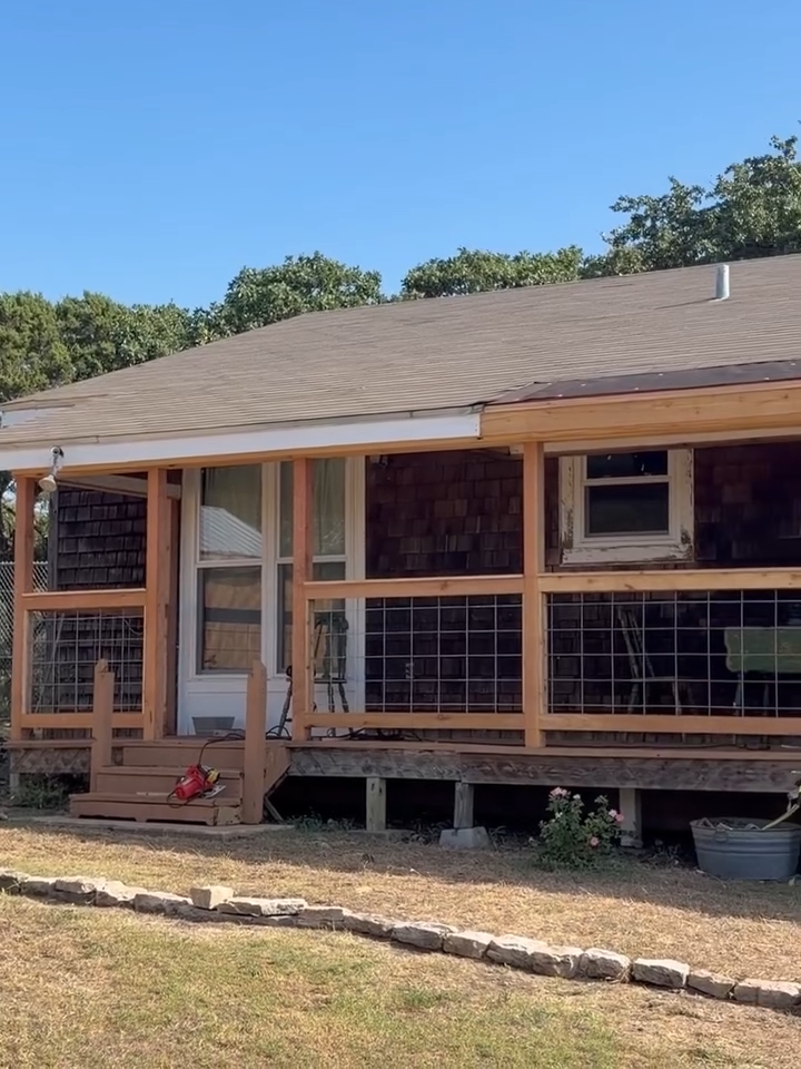 Front porch of a wooden house with screened windows, gray roof, and a small brick step under a blue sky