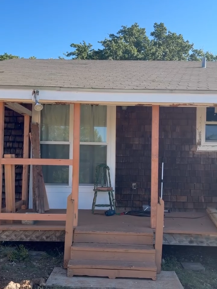 Front porch with unfinished wooden steps and railings on a house, with tools and ladders visible inside.
