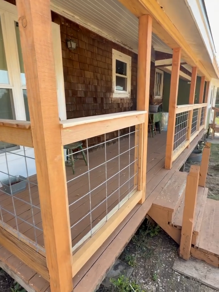 Wooden porch with wire railing and steps beside a brown house, viewed from the corner.