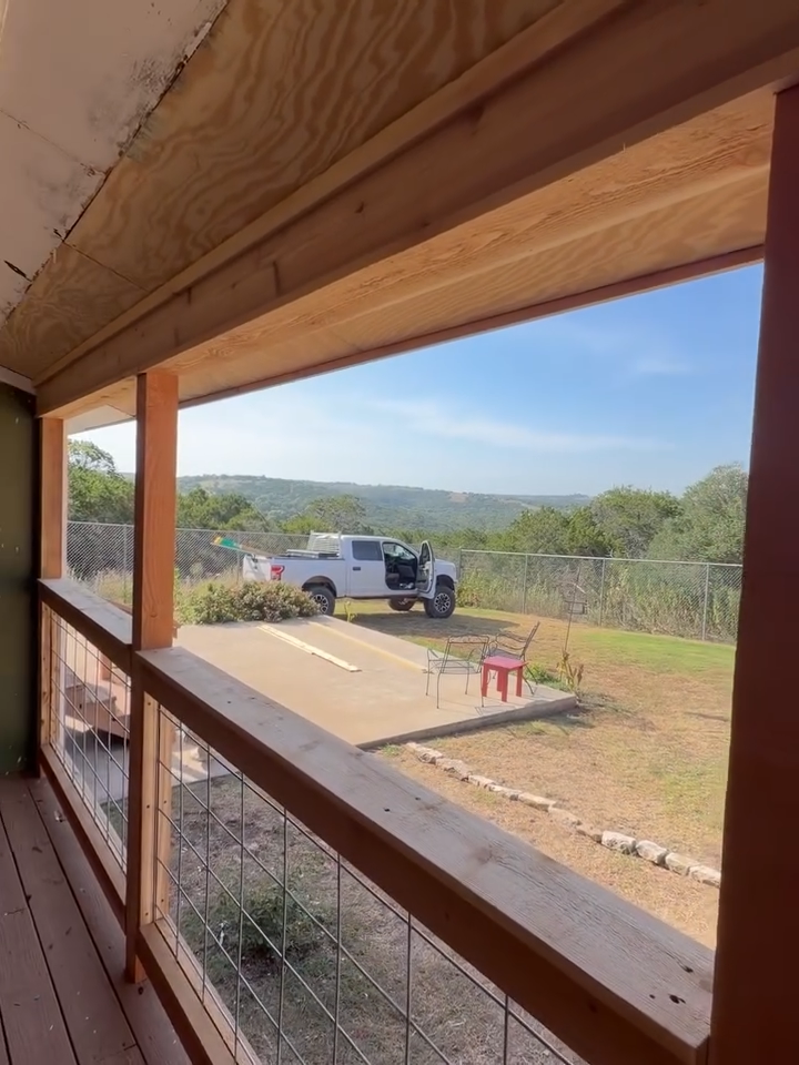 Wooden porch overlooking a fenced yard with a white pickup truck and red chair on a concrete slab.