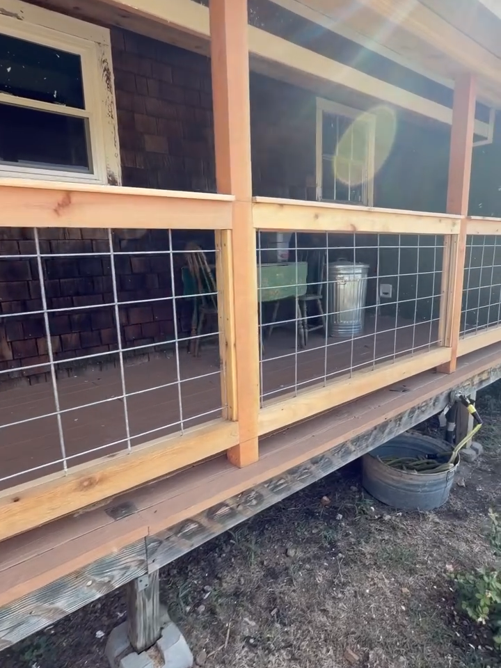Wooden porch under construction with wire mesh railing and a window, raised on cinder blocks.