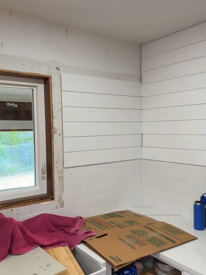 Partially renovated white room with window, pink cloth, cardboard on floor, and blue bottle on right