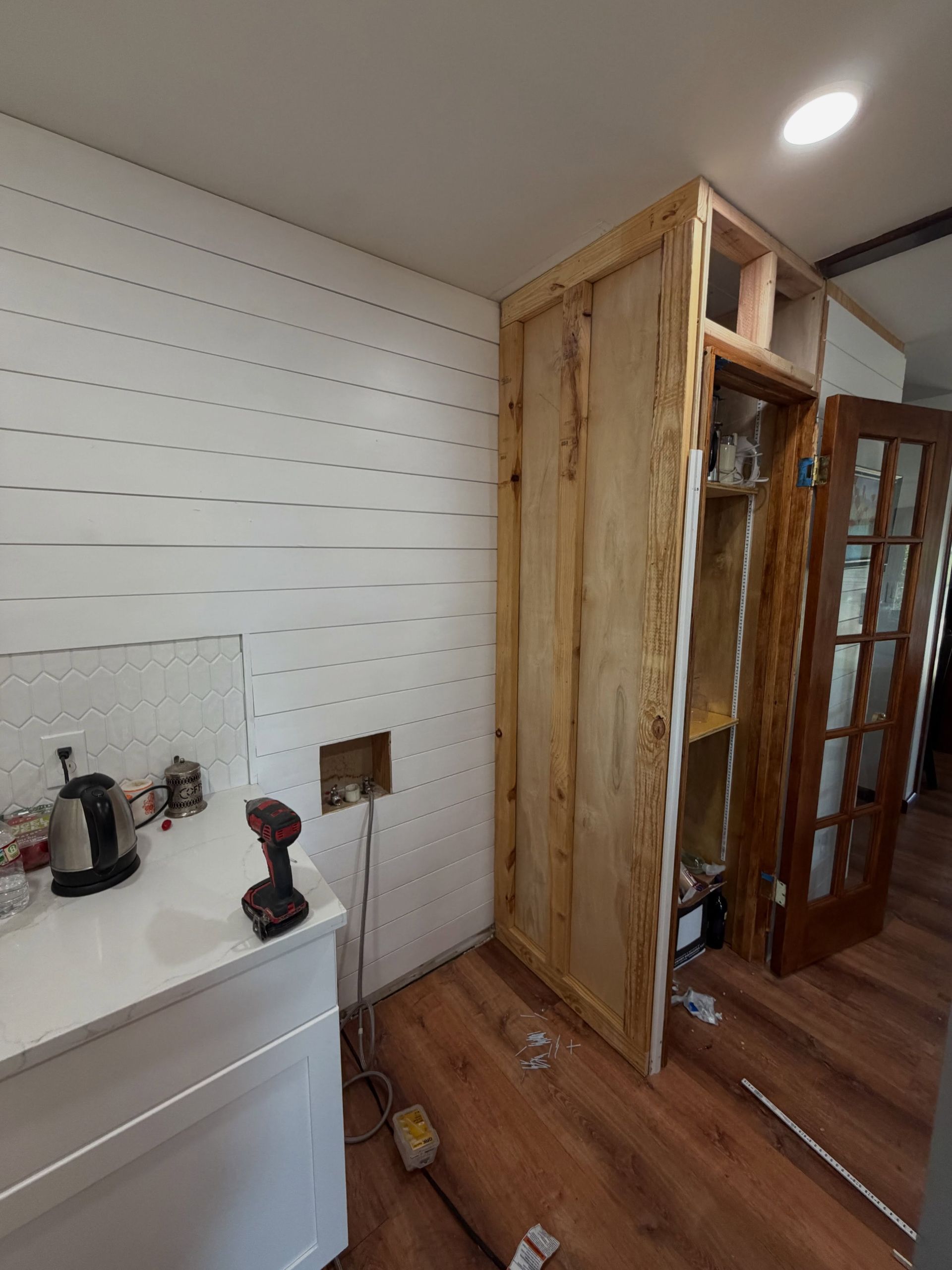 Small room with wood wardrobe, wall-mounted pegboard, and chest with kettle and tools on it.