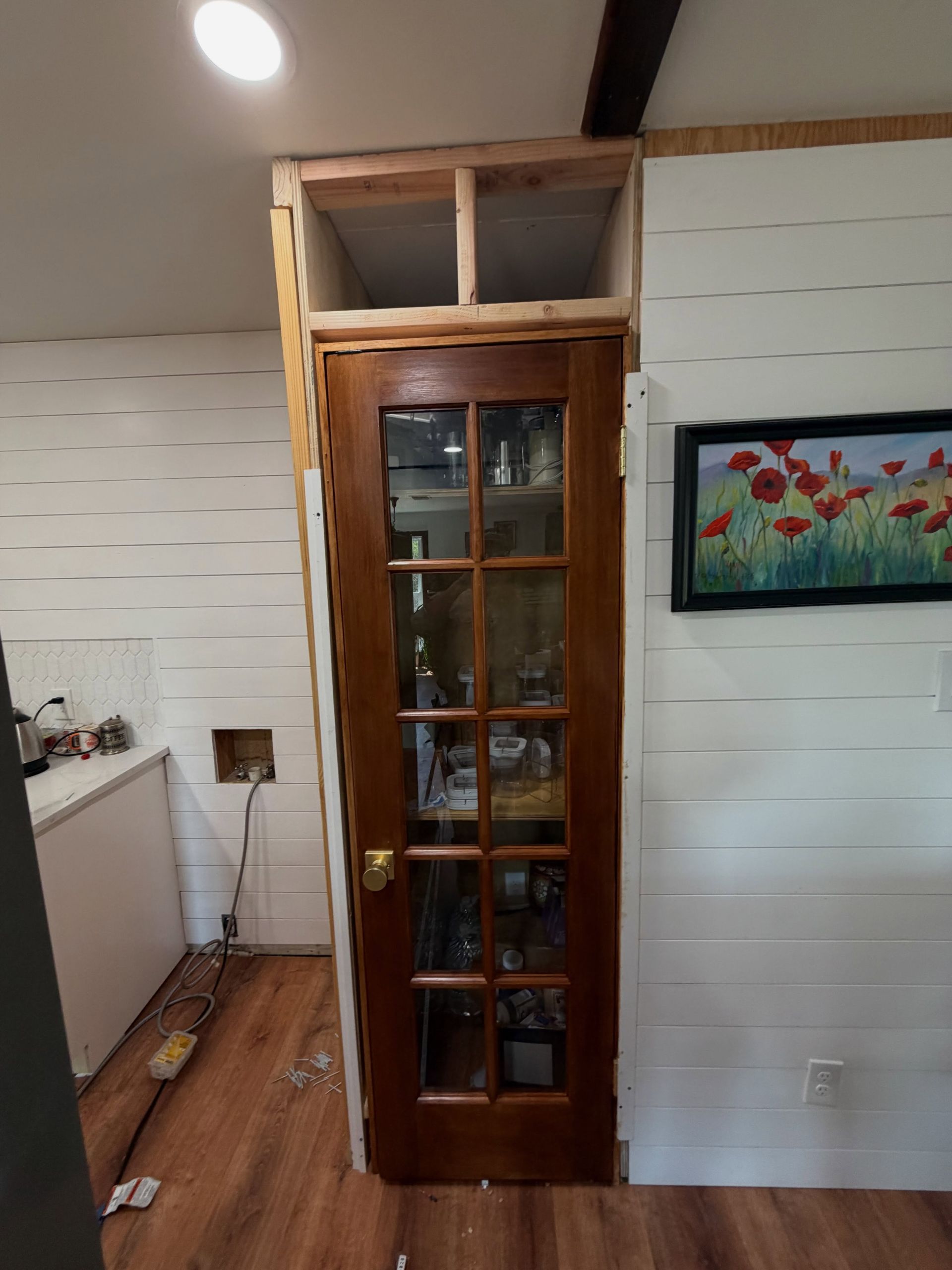 Wooden glass-paneled door in a white interior hallway, with framed floral art on the wall.