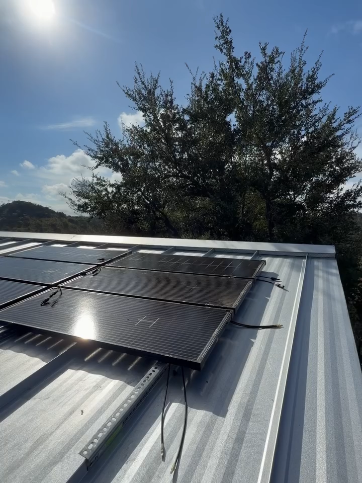 Solar panels mounted on a metal roof under a bright sky, with a tree in the background