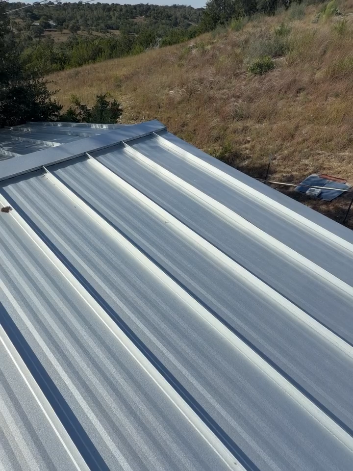 Corrugated metal roof panels with a wooded hillside in the background