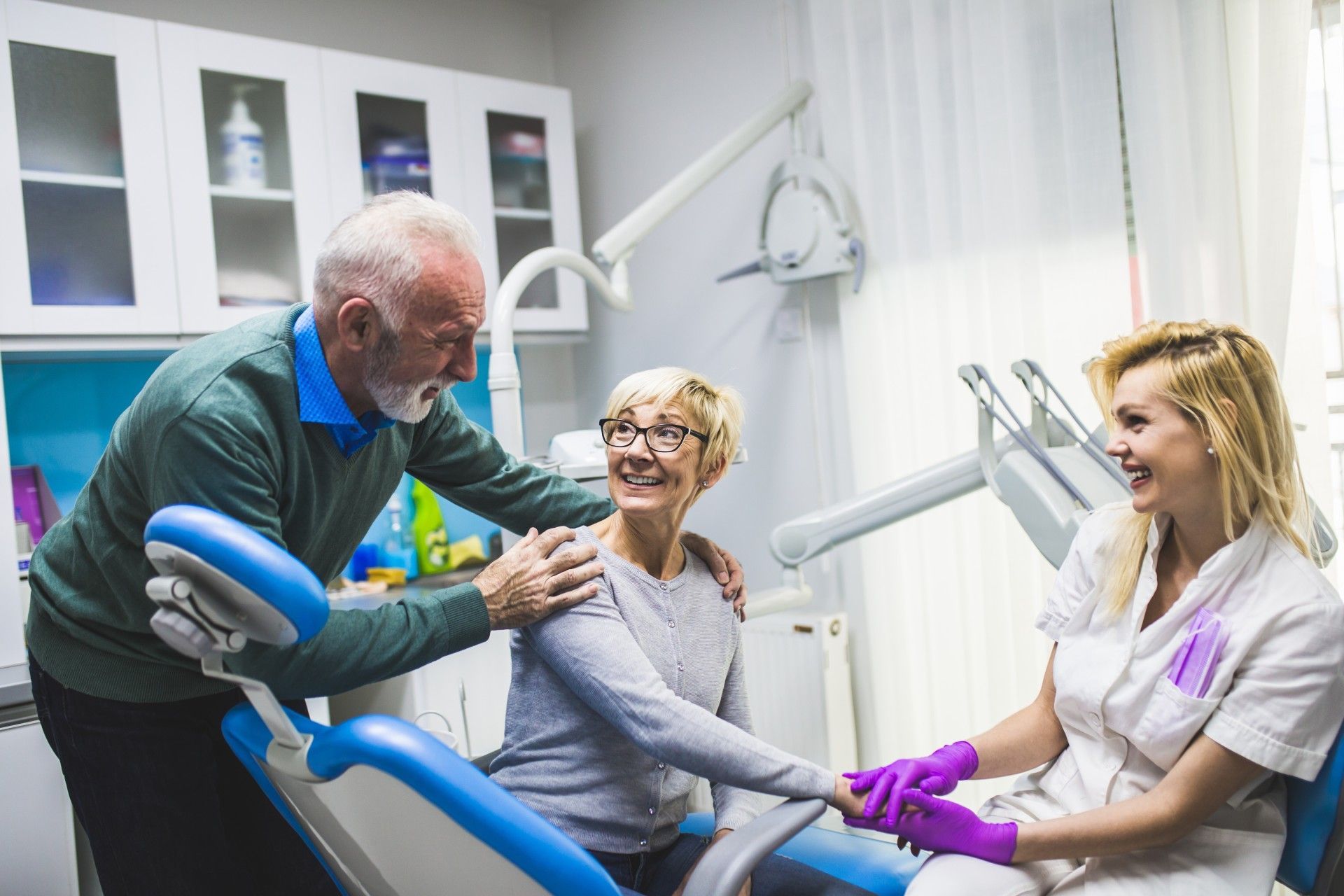 An elderly couple is sitting in a dental chair talking to a dentist.