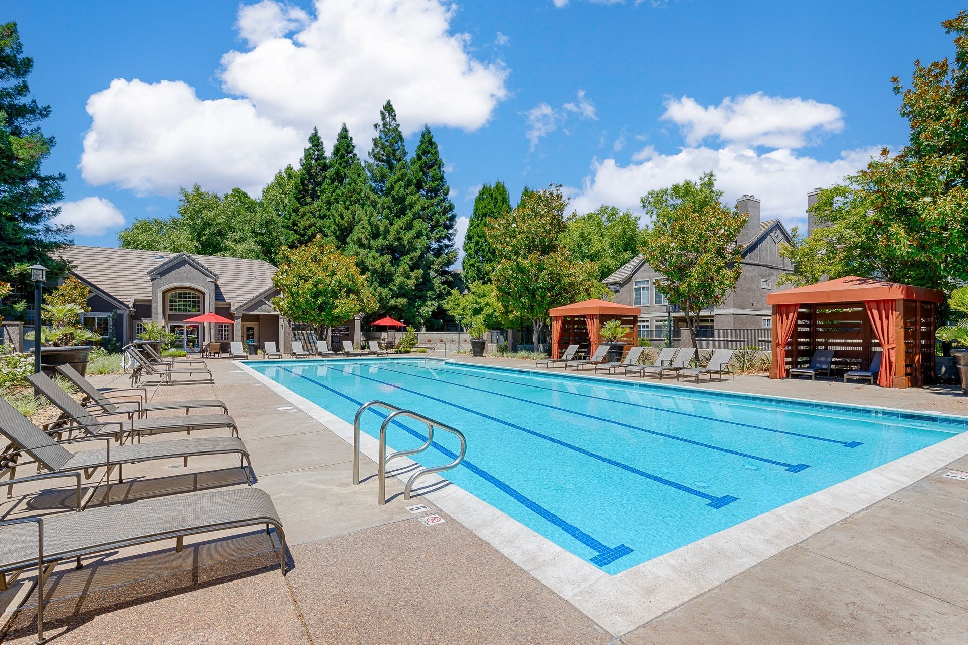 Outdoor community pool with lounge chairs and orange cabanas under a blue sky.