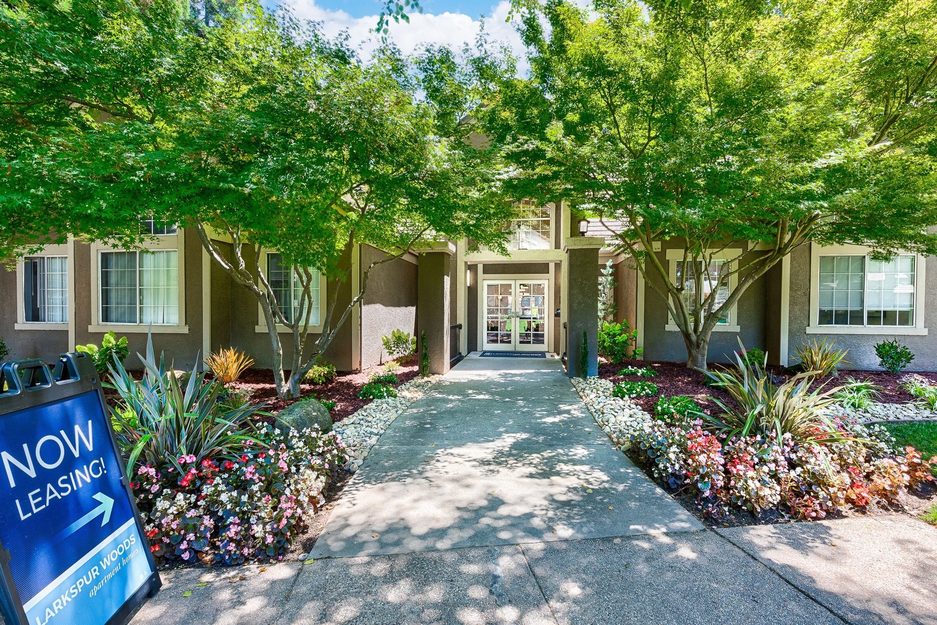 Accessible walkway to apartment building entrance with trees and landscaping.