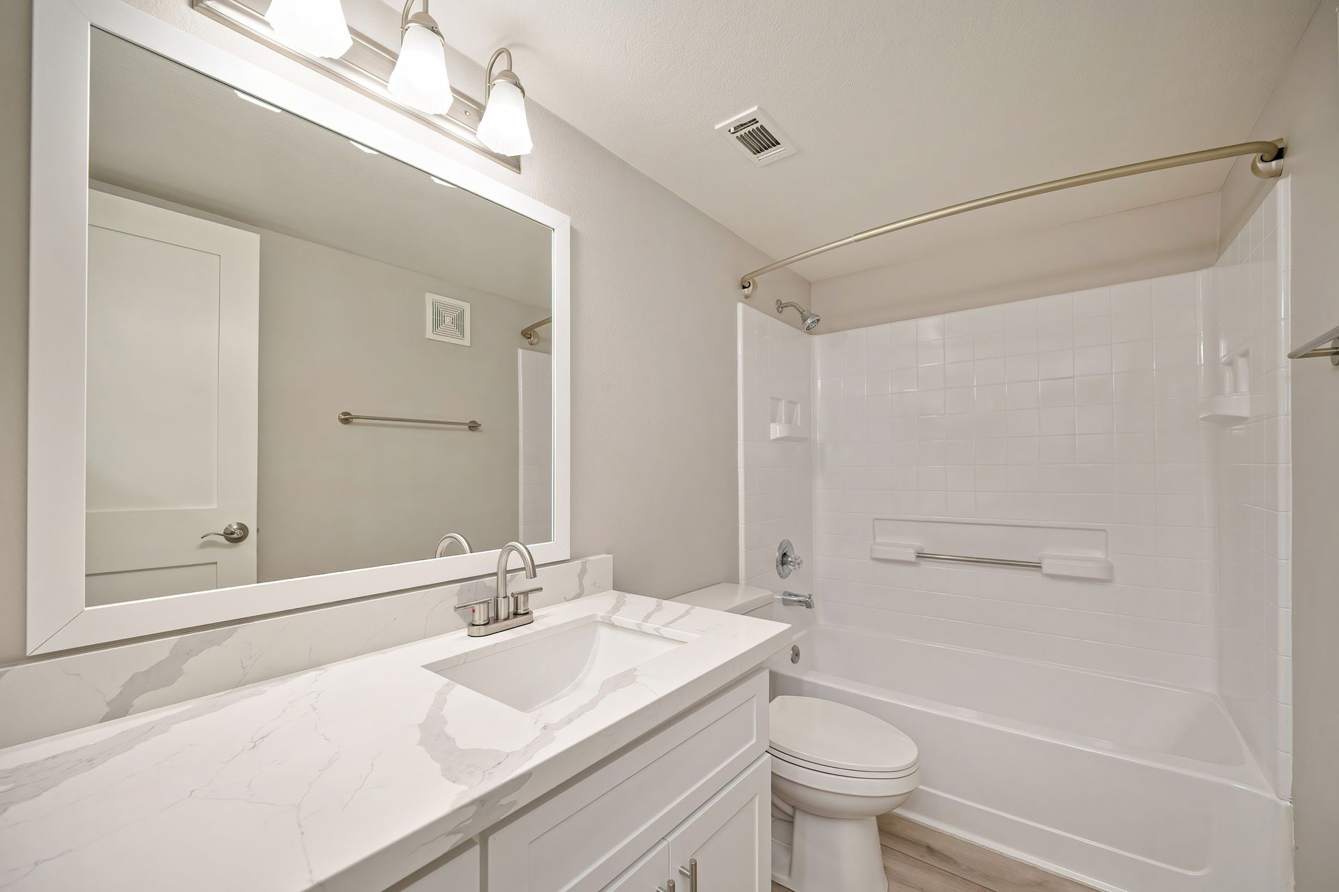 Bright white bathroom with vanity, large mirror, and shower-tub combo with grab bars.