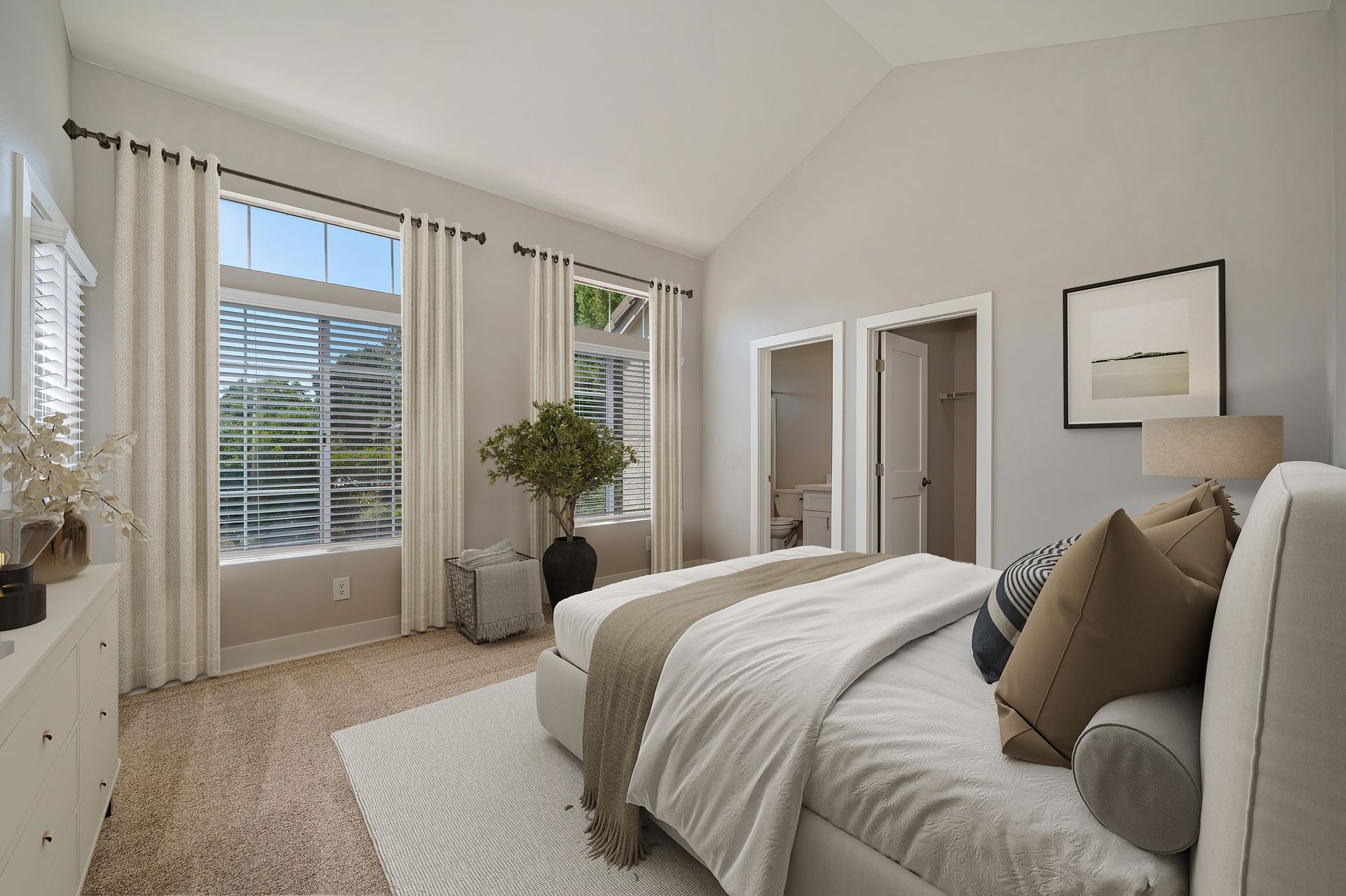 Bright bedroom with white bedding, tall windows, sheer curtains, and a potted plant near the corner.