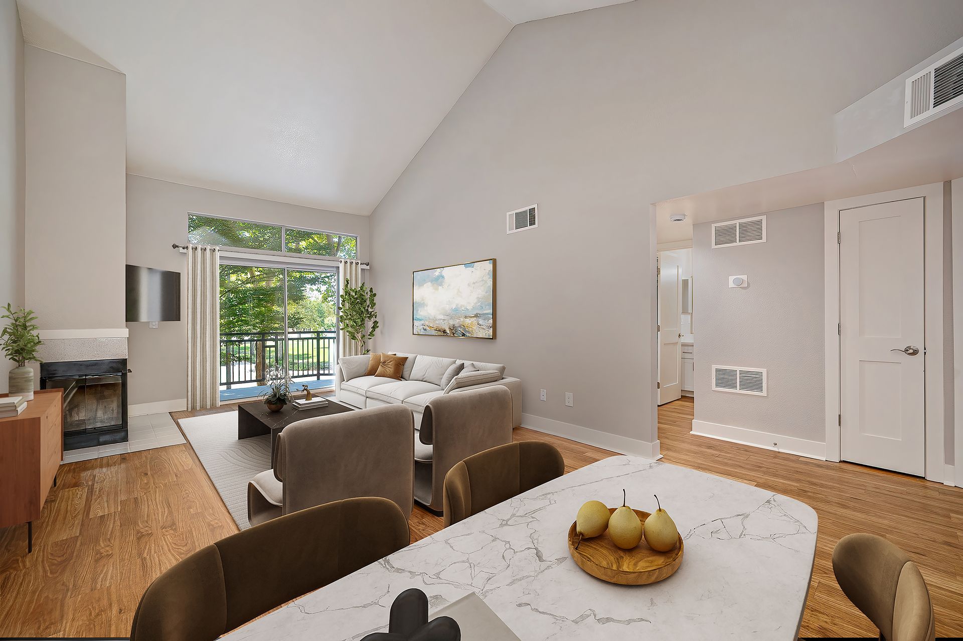 Bright modern living room with vaulted ceiling, marble table, brown chairs, and large glass doors to greenery