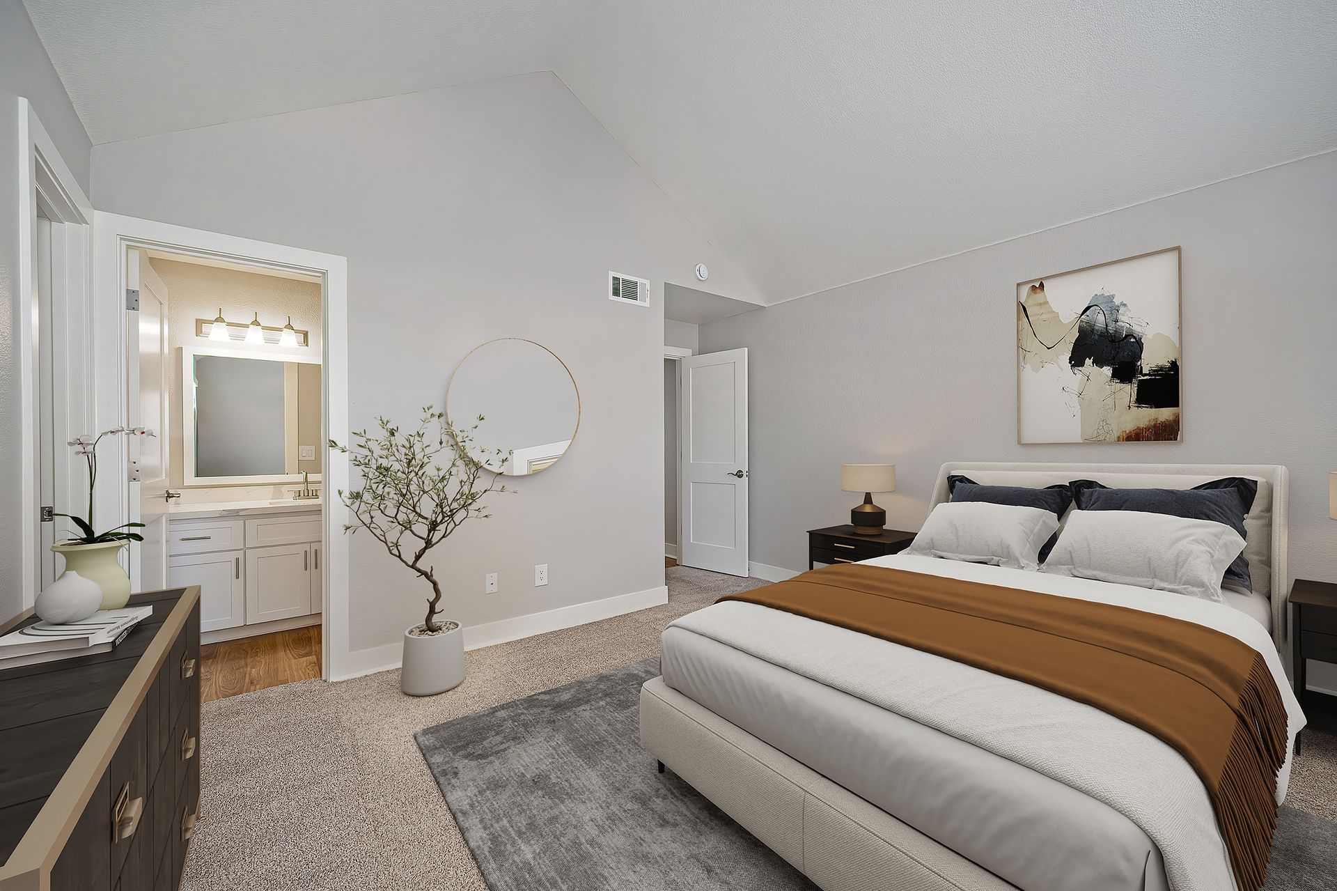 Bright modern bedroom with a bed, gray rug, dresser, mirror, and bathroom doorway.