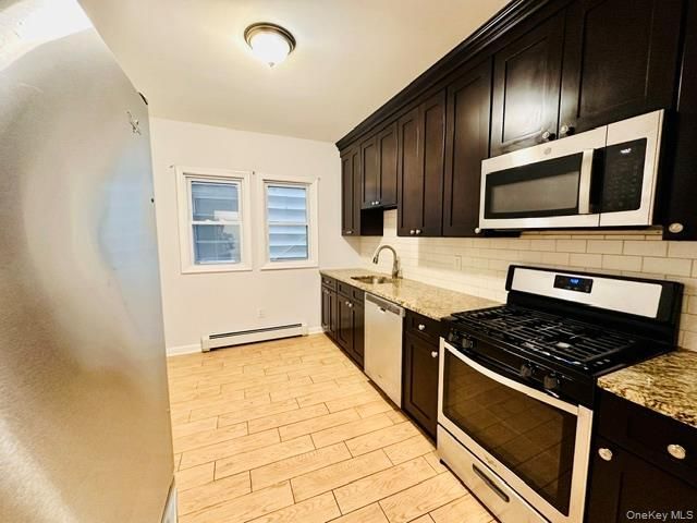 Bright kitchen with dark cabinets, stainless steel appliances, and tiled floor by two windows