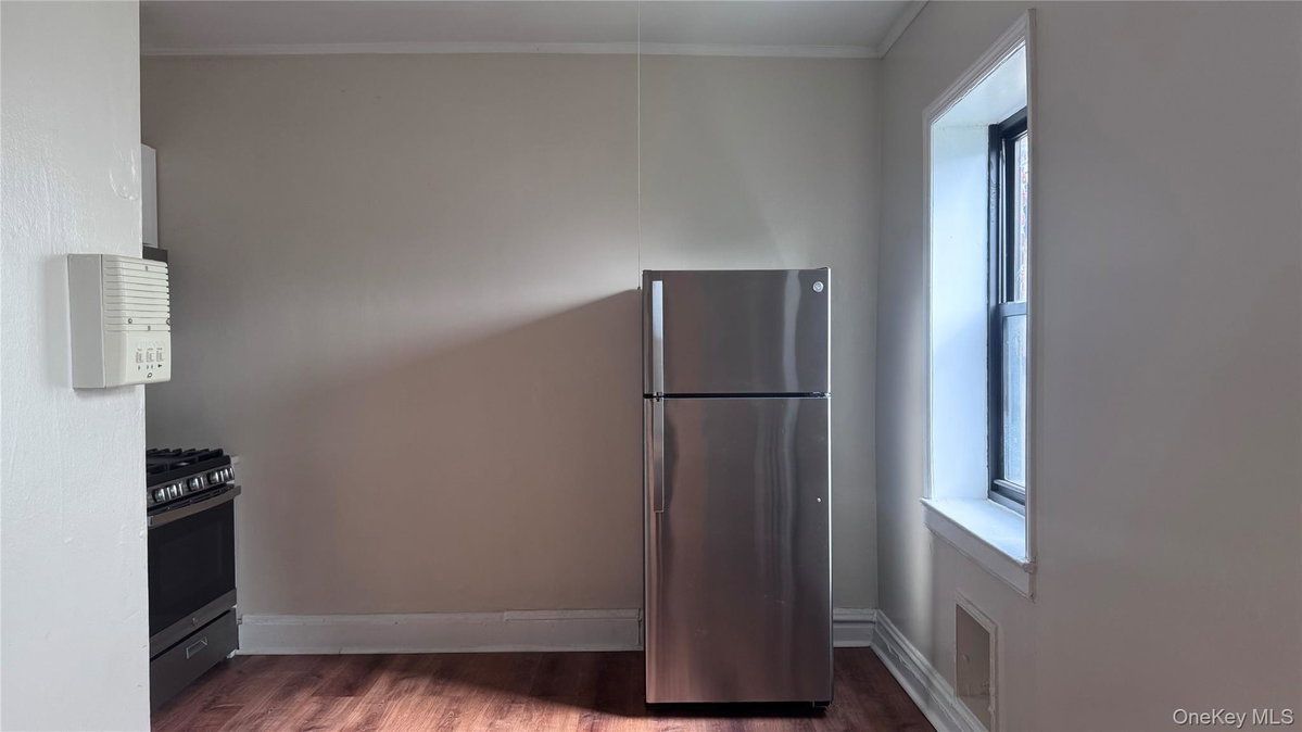 Empty kitchen with a stainless steel refrigerator and a bright window on the right.