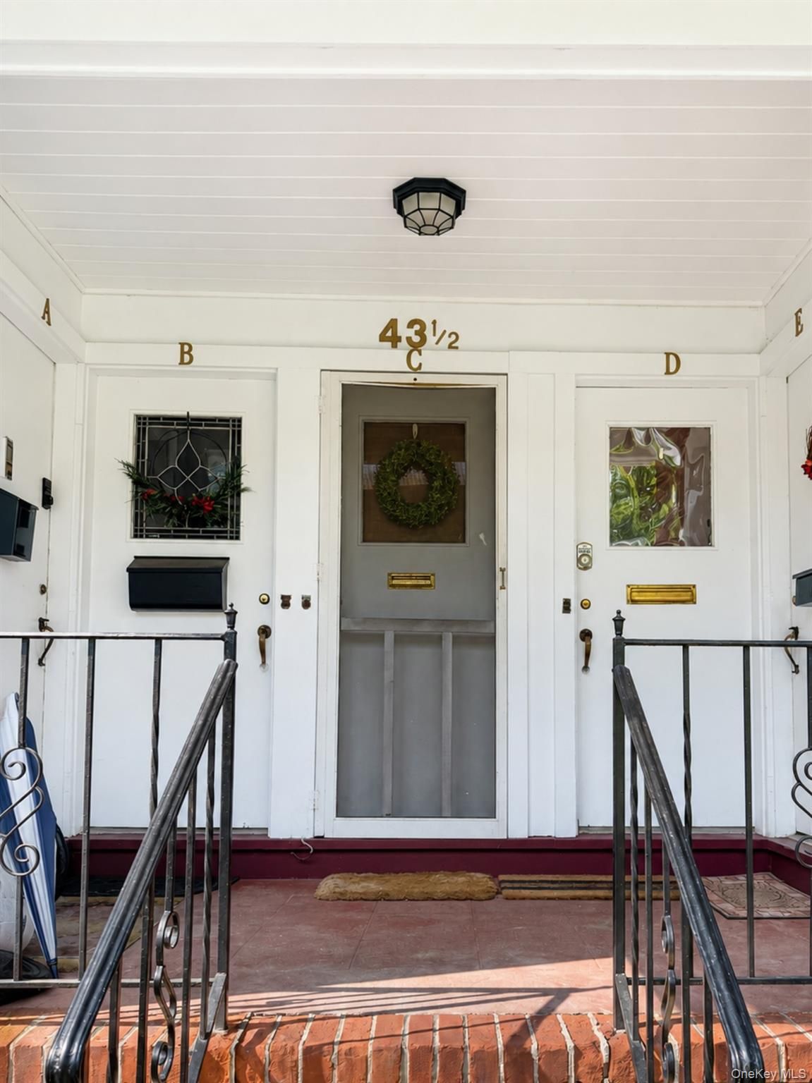 Front porch of a white house with door 43½, windows B and D, black railings, and a wreath on the door