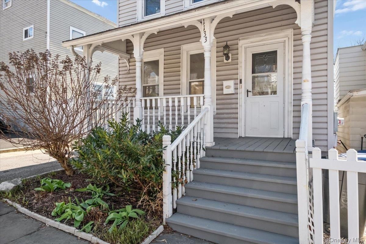 Front porch of a gray house with white trim, stairs, railing, and potted greenery