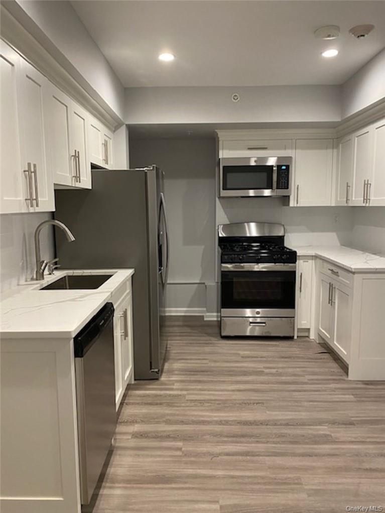 Modern kitchen with white cabinets, stainless steel appliances, gray walls, and wood-look flooring
