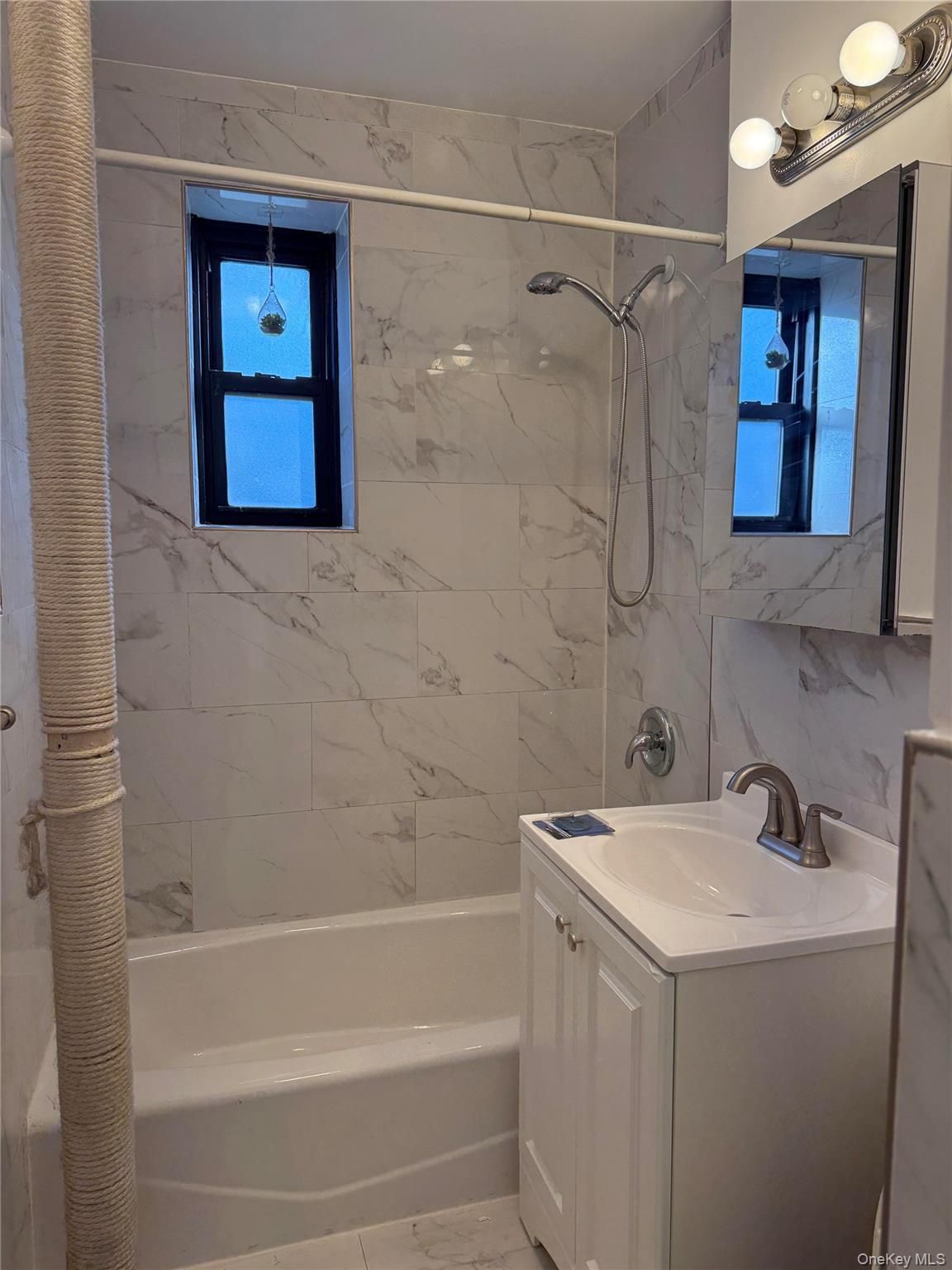Small bathroom with white marble tile, bathtub, vanity sink, and two narrow windows.