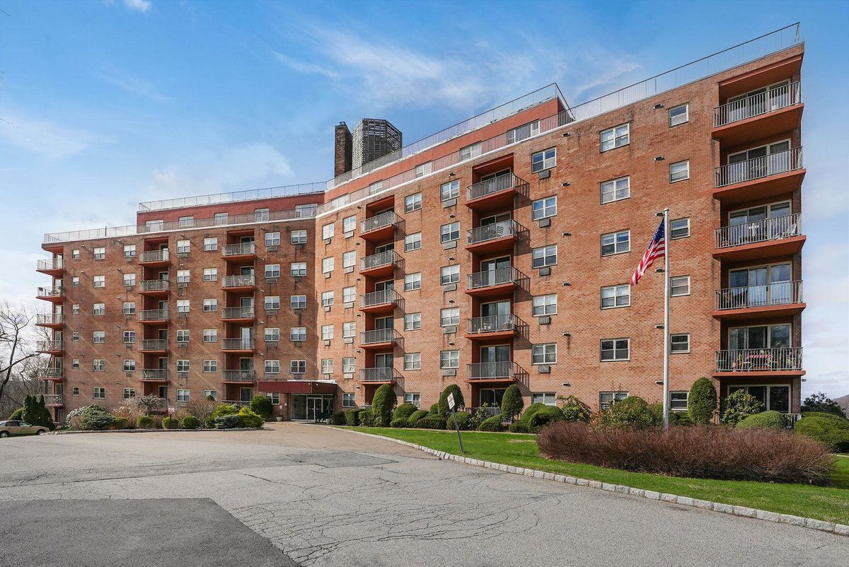 Brick apartment building with balconies, a driveway, and an American flag at the entrance