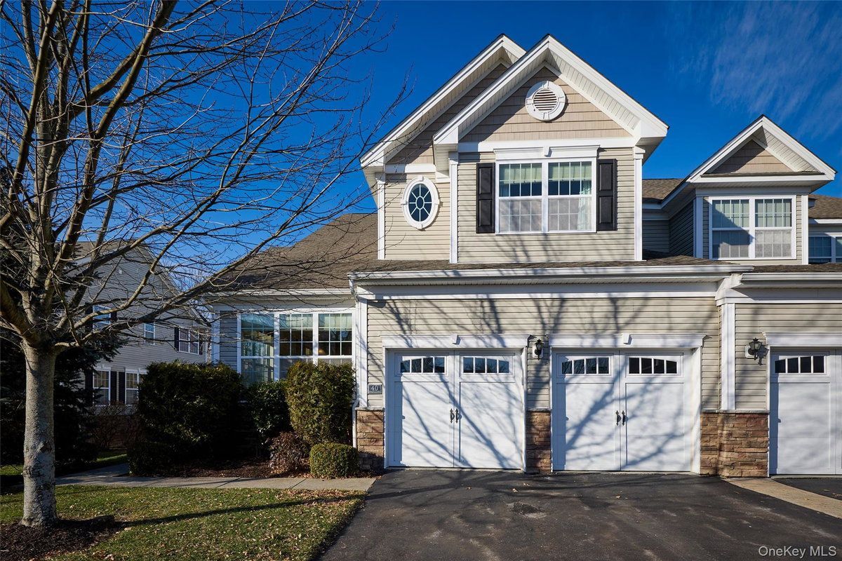 Suburban house with two-story garage, white siding, and bare tree under a clear blue sky