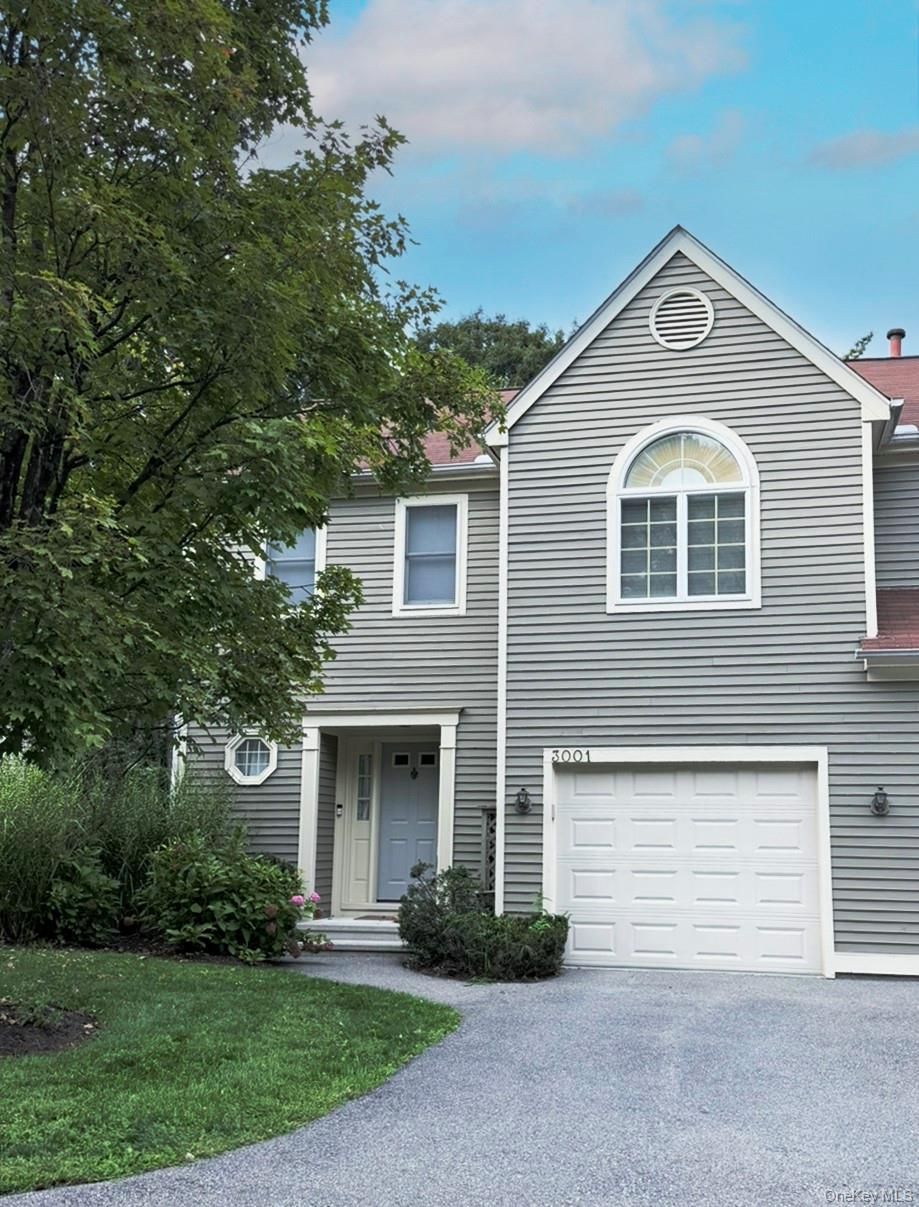 Gray two-story house with white trim, garage, and gravel driveway beside trees and lawn