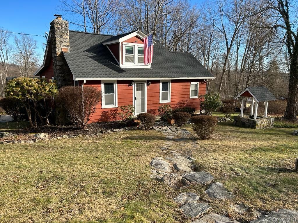 Red brick house with black roof and dormer, front yard, and a stone-lined path under bare trees.