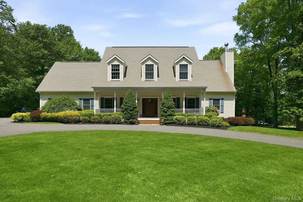 Suburban house with gray siding, white trim, and a large green lawn under a clear sky