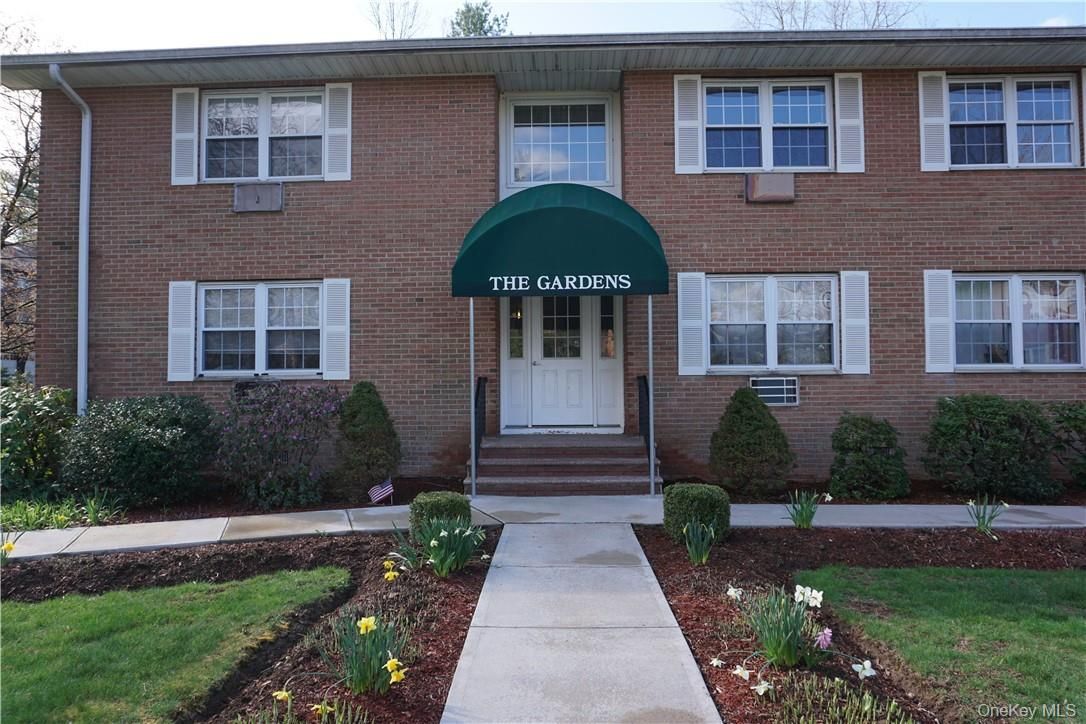 Brick apartment building entrance with green awning and walkway leading to the door