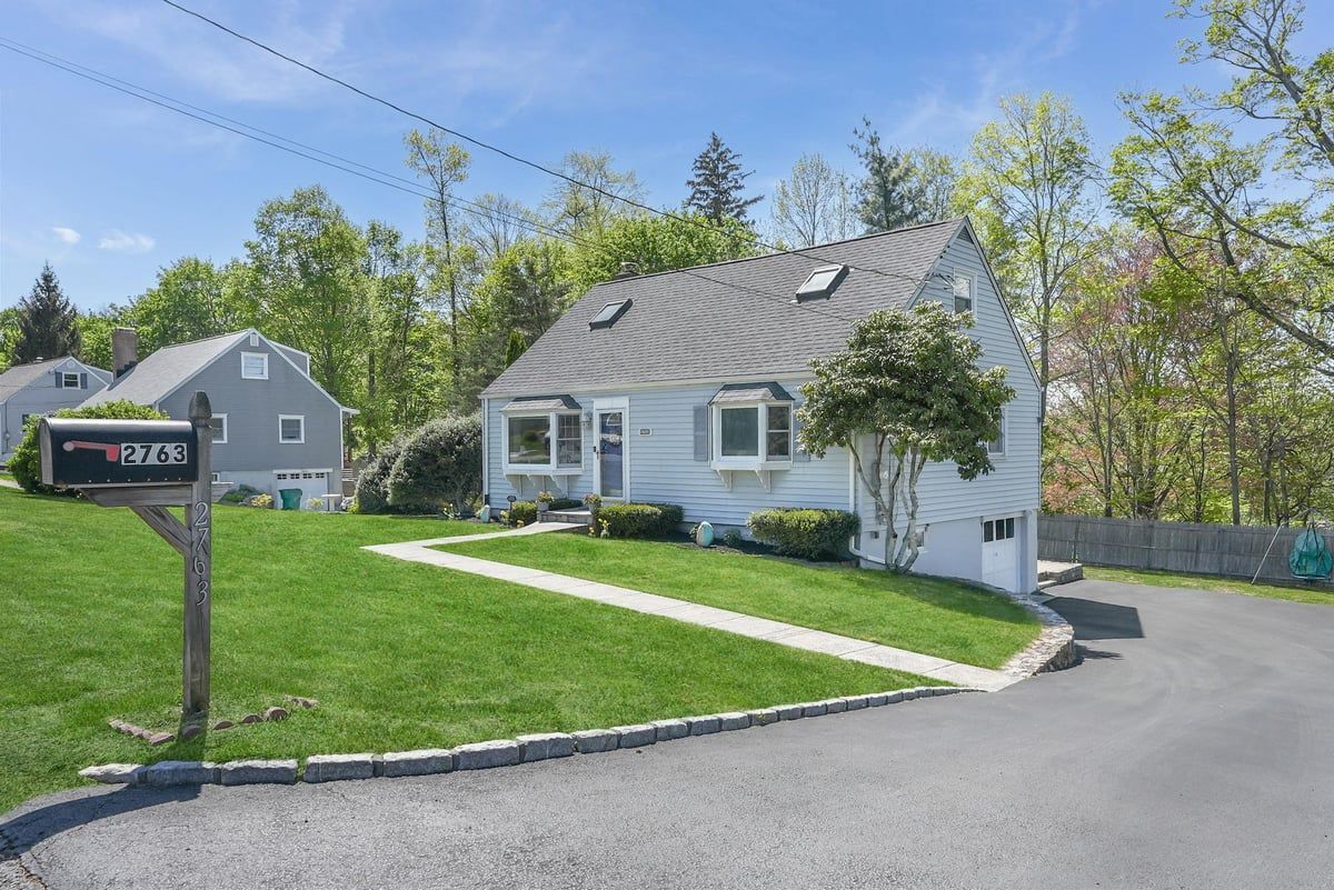 White cottage with green lawn and driveway, seen beside a mailbox under a blue sky