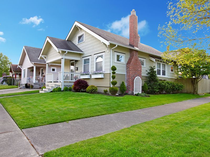 Suburban house with a red brick chimney, green lawn, and sidewalk under a blue sky