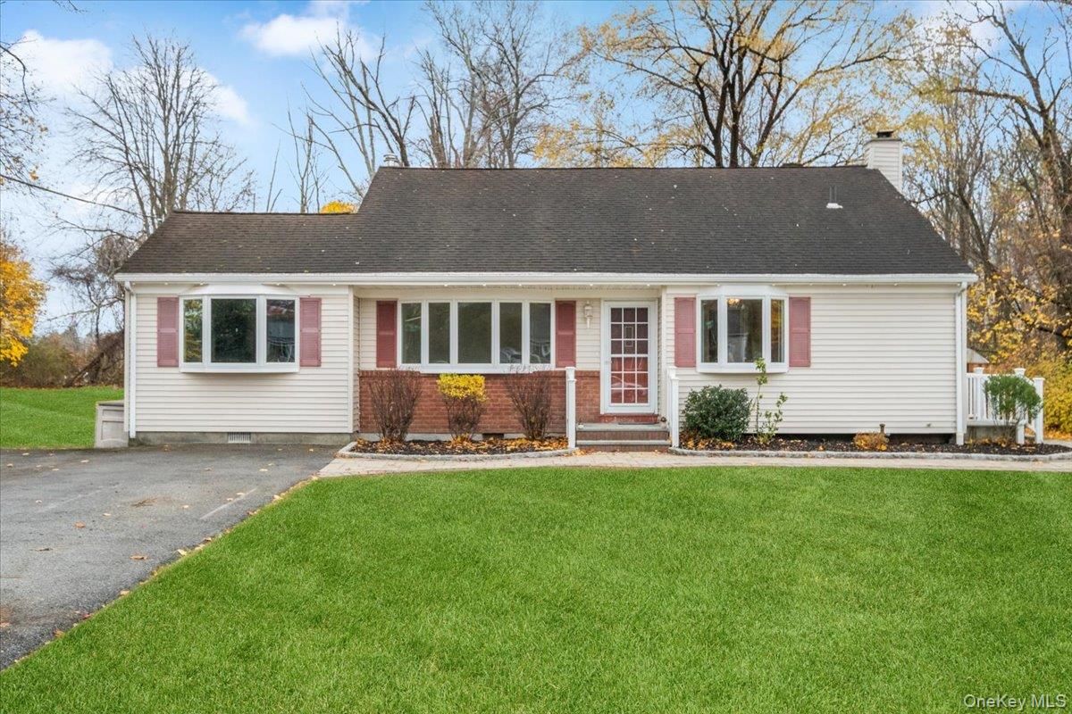Single-story white house with red shutters, front porch, driveway, and green lawn in autumn.