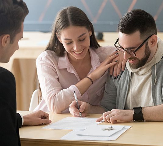 Three people collaborate at a desk, smiling and reviewing papers in a bright office.