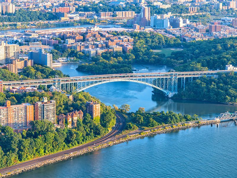 Aerial view of a city with a river, bridge, apartment buildings, and green parks along the waterfront