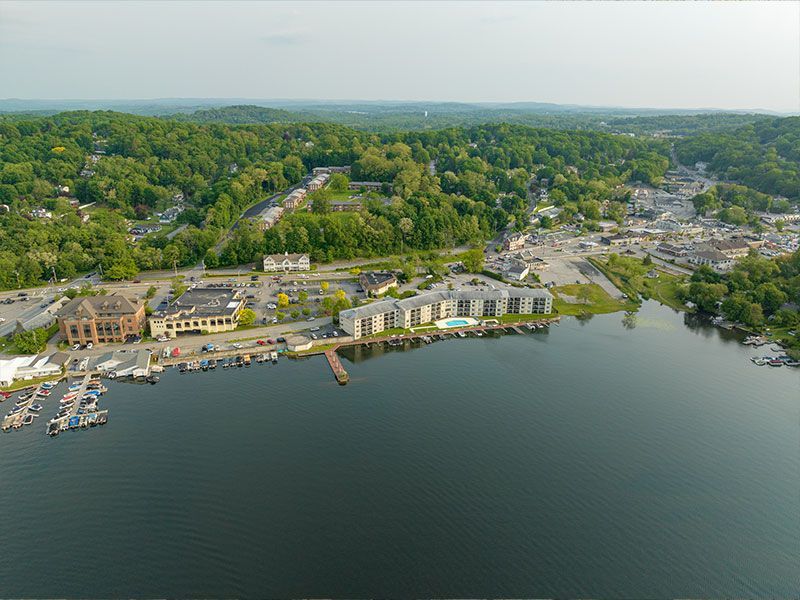Aerial view of a lakeside town with docks, buildings, and tree-covered hills along the shoreline.