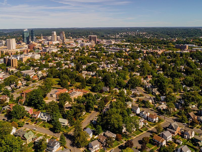 Aerial view of a leafy suburban neighborhood beside a downtown skyline under clear skies