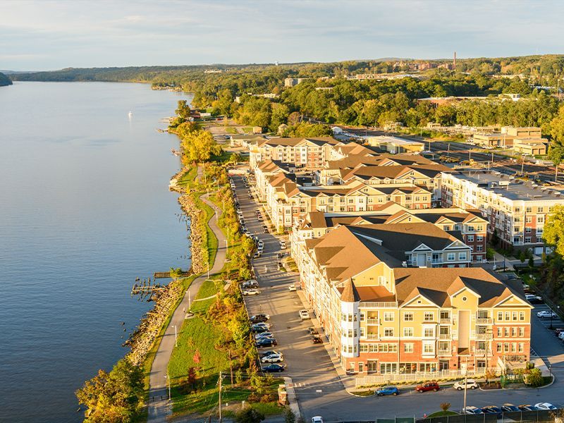 Aerial view of waterfront apartment buildings beside a calm lake with a shoreline path and green trees