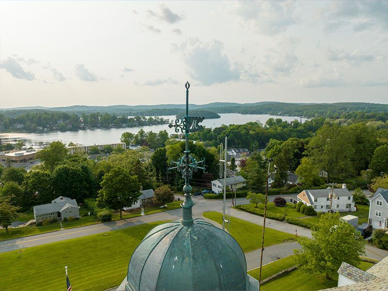 View from a dome-topped tower over a green town, river, road, and distant hills under a cloudy sky.