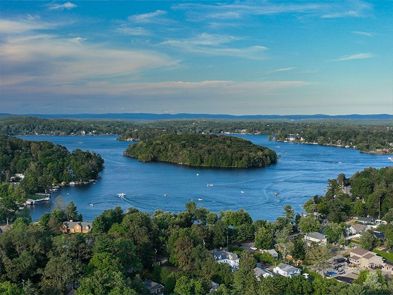 Aerial view of a blue bay with a tree-covered island and houses along the shore under a clear sky