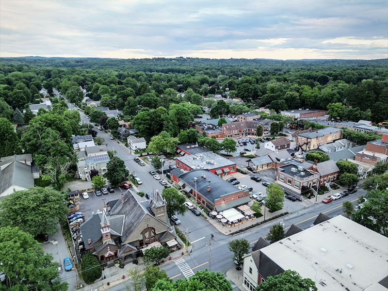 Aerial view of a small town street lined with buildings and trees under a cloudy sky