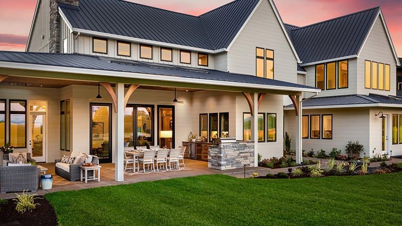 Modern two-story house with lit patio, white trim, and a manicured lawn at dusk
