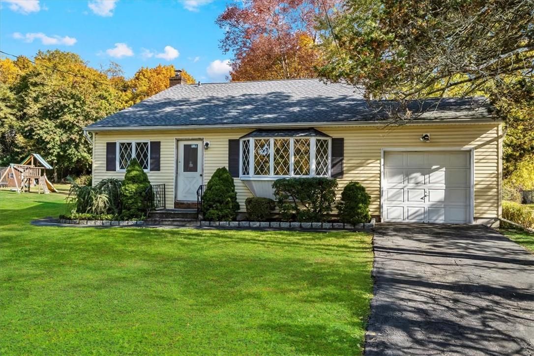 Single-story cream house with white garage, front lawn, and autumn trees.