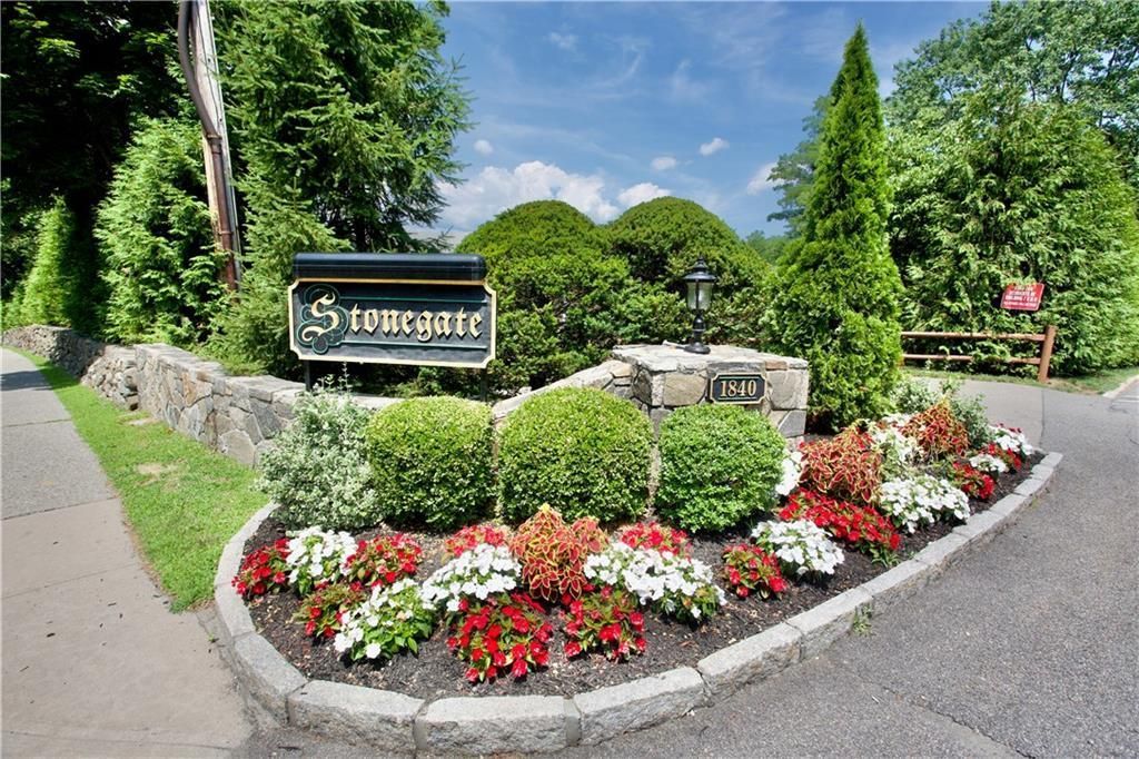 Welcome sign surrounded by colorful flowers at the edge of a paved road and green landscaping