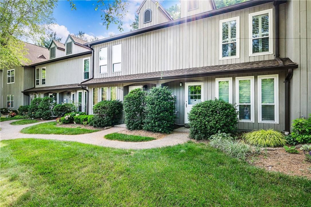 Two-story beige townhouse with green lawn and shrubs on a sunny day