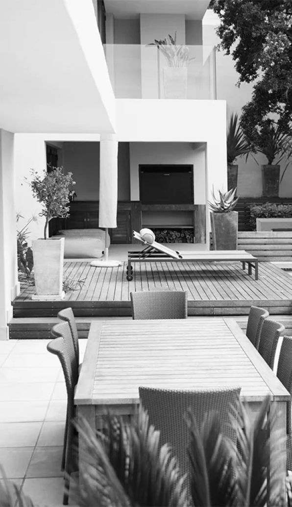 Modern patio with outdoor dining table, wicker seating, and a pool beside a contemporary house