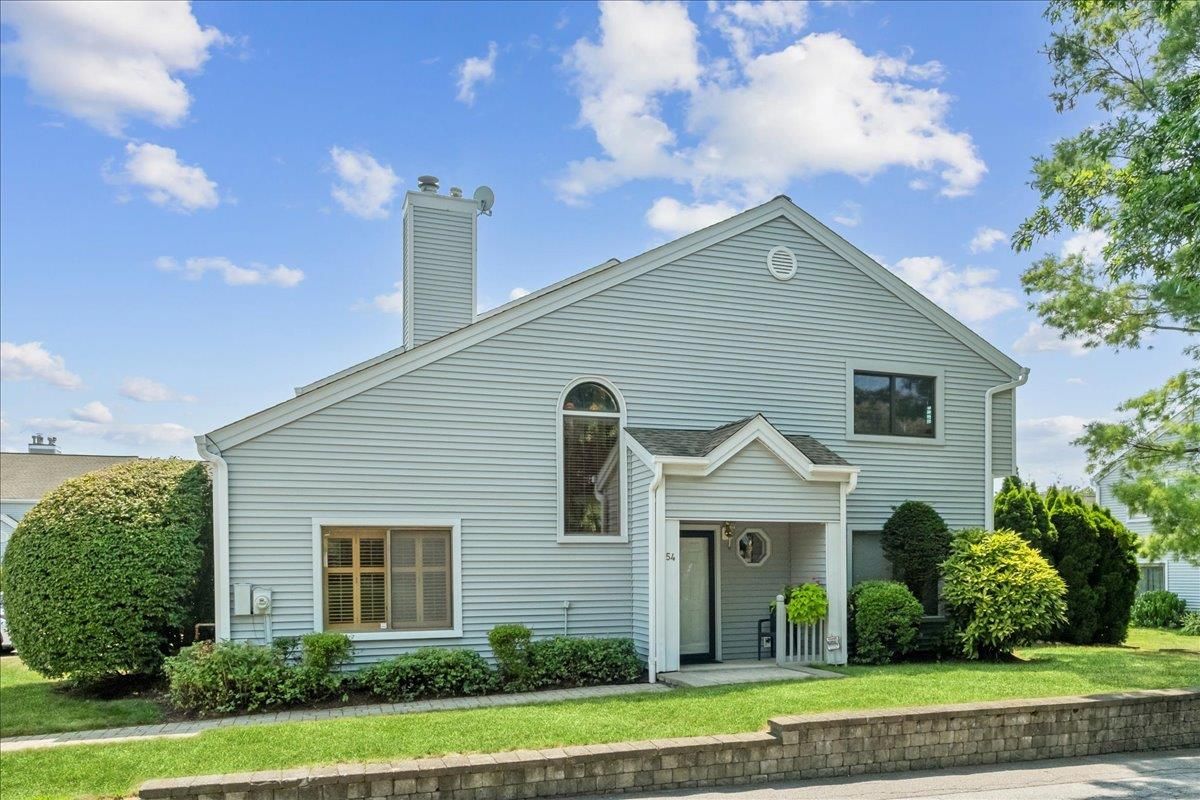 Light blue suburban house with white trim, front porch, and manicured shrubs under a bright sky